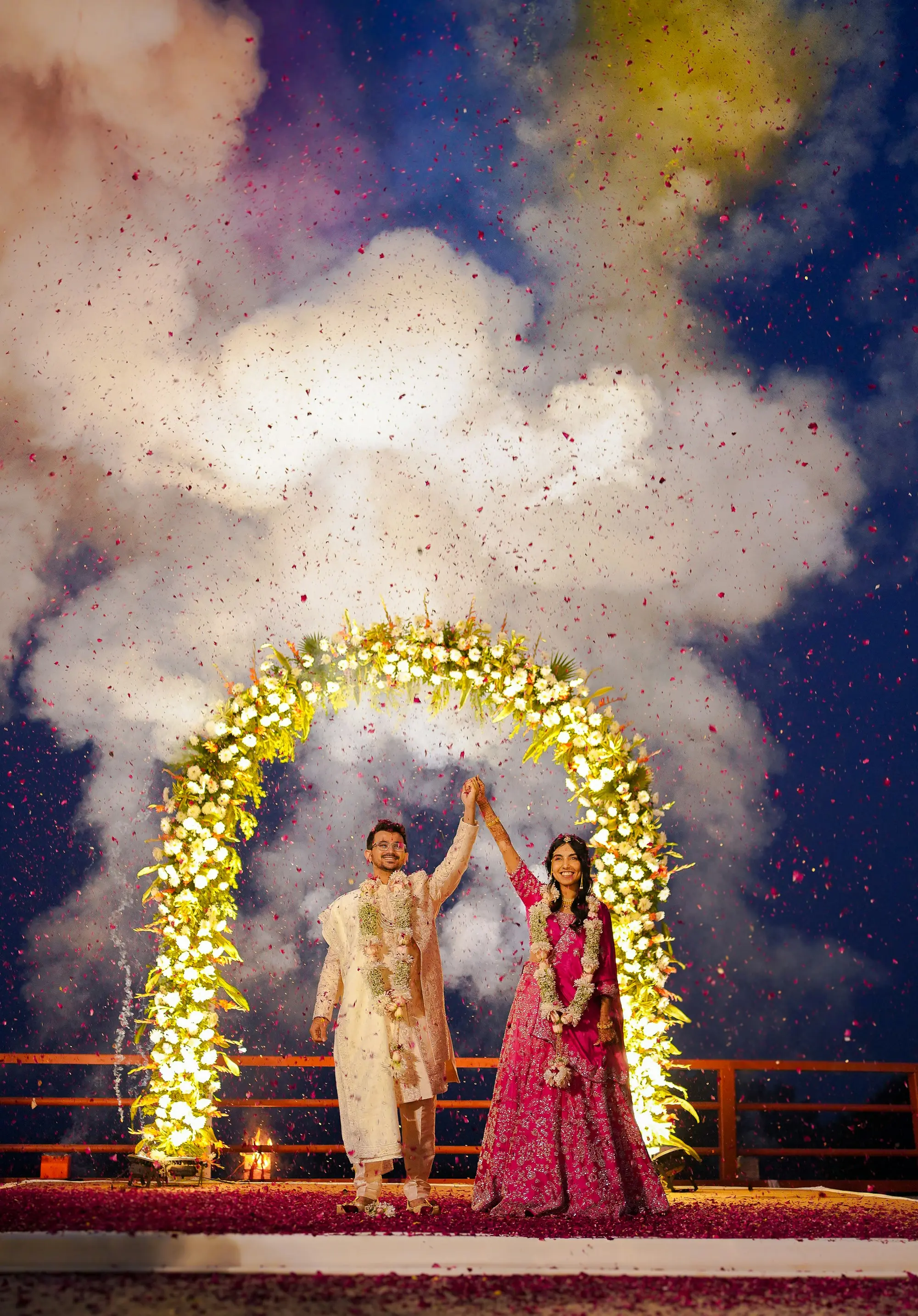 Couple celebrating under a floral arch with confetti