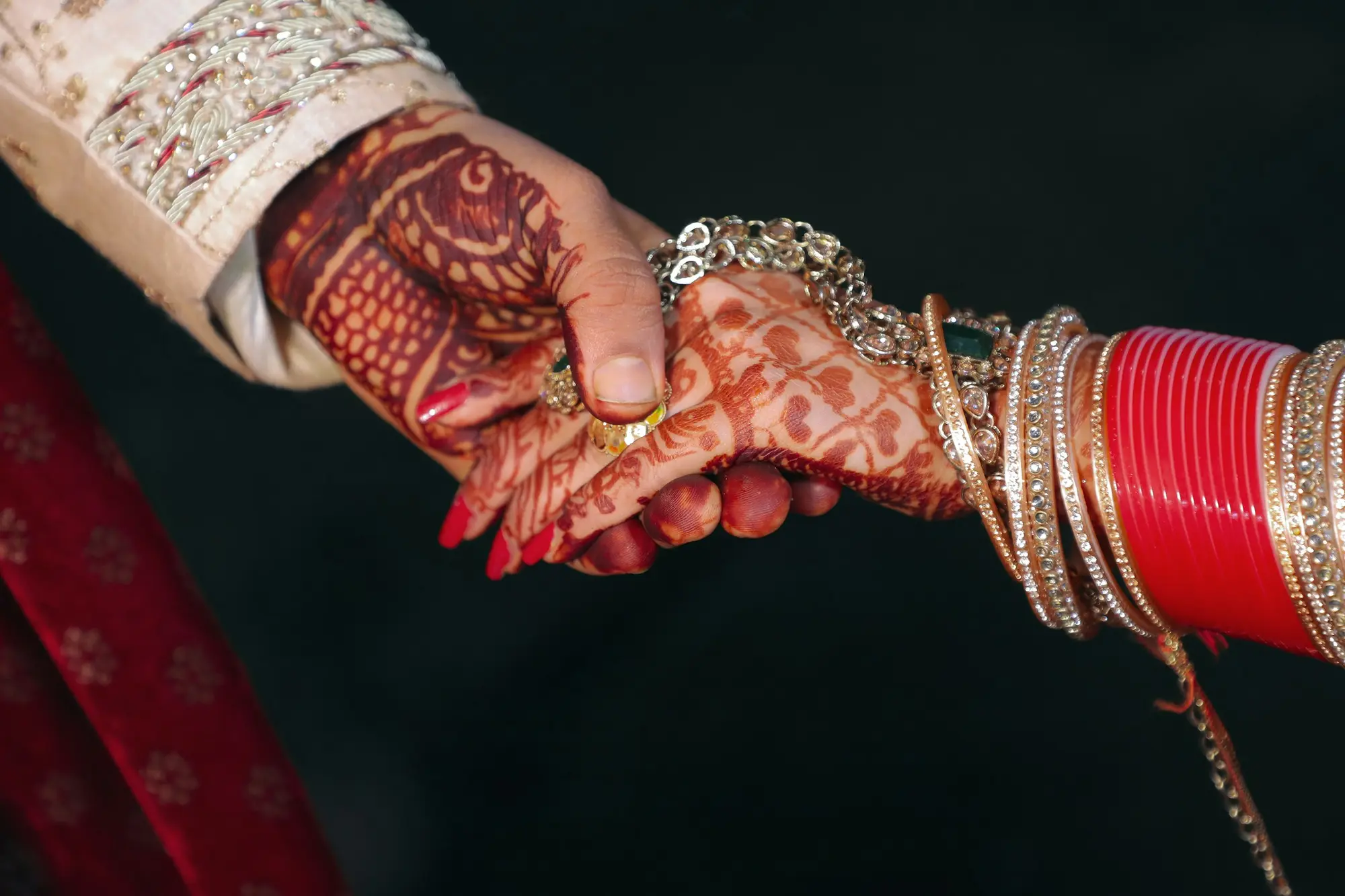 Bride and groom holding hands, bride's hands adorned with henna and red bangles